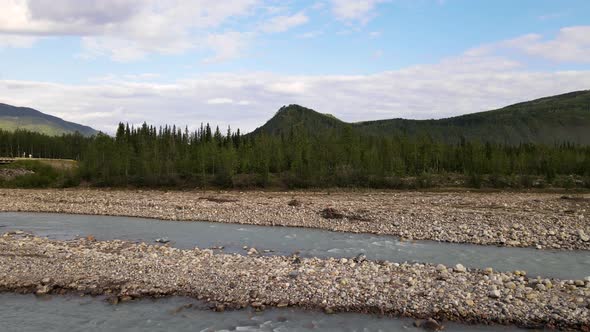 Banks of Toad River with a green hill and forest at the background in Northern British Columbia, Can