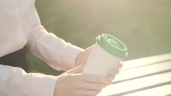 Beautiful business woman in a shirt and black skirt sits on a park bench with a disposable cup of co