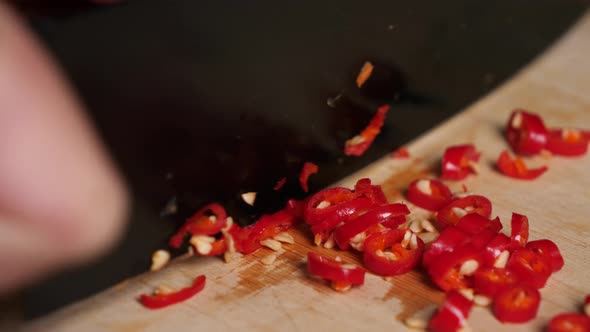 Extreme close up chopping a red chili pepper with a black knife on wooden board.