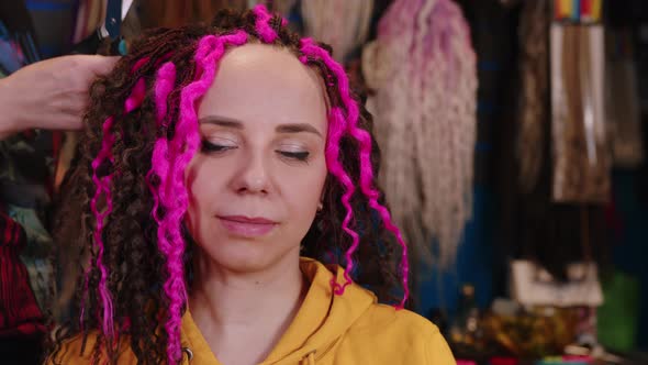 Unrecognizable person makes curly hairstyle for young woman in salon.