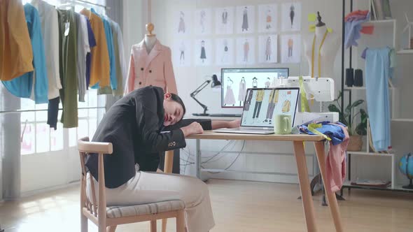 Back View Of Asian Female Designer In Business Suit Sleeping While Designing Clothes On A Laptop