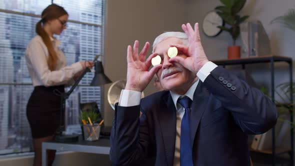Elderly Man Boss Dancing Fooling Around Making Silly Faces with Bitcoin Coints Eyes in Office