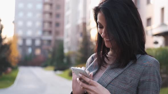 Portrait of a Confident Business Woman in a Suit Uses a Smartphone Outdoors