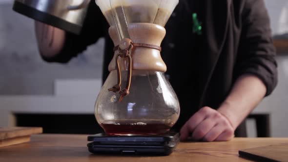 Barista pouring hot water into filter with coffee. Brewing coffee in a chemex