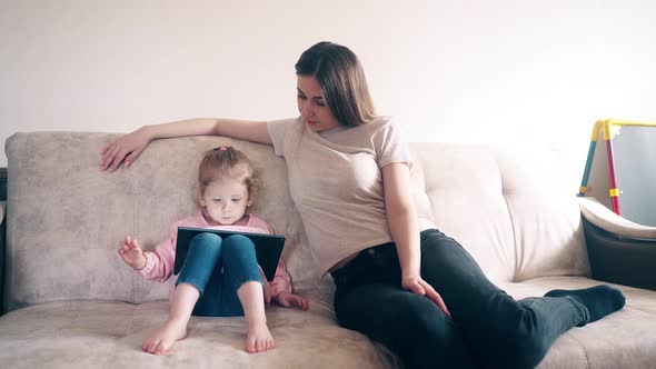 Young Mother and Daughter Are Sitting on the Couch and Training Using a Tablet Computer