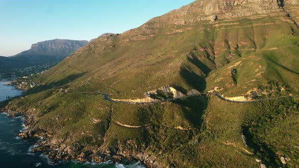 Chapmans Peak road coastline during sunset with table mountain in background, aerial