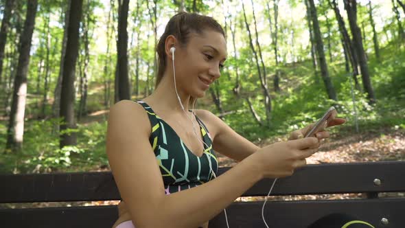Gorgeous Fitness Texting on Smartphone and Listening To Music on White Earphones