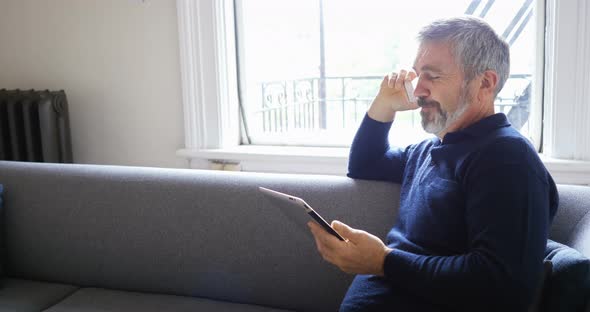 Man talking on mobile phone while using digital tablet in living room 4k