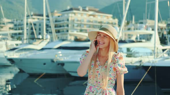 Elegant Woman Speaking on Smartphone on the Street with Yachts in the Background