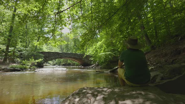 Man Sits Next to Boulder Bridge In Rock Creek Park - Washington, DC - Springtime