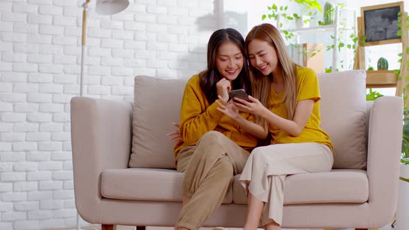 Young Asian lesbian couple  having fun using digital device while relaxing on couch in the living ro
