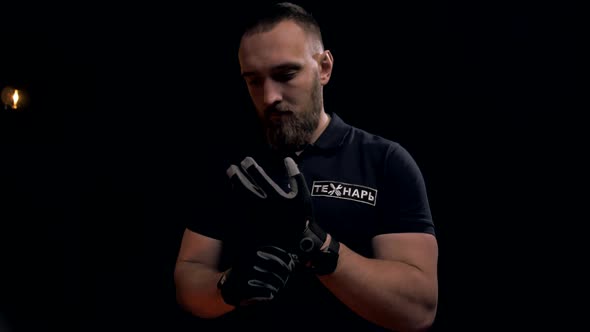 Professional worker with a beard puts on gloves before work. Black background