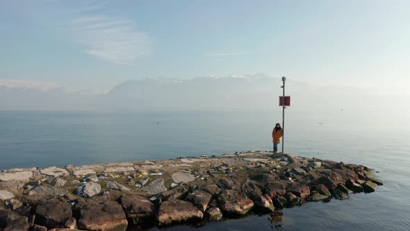 Aerial dolly of woman standing at the edge on stone quay at lake Geneva, Switzerland