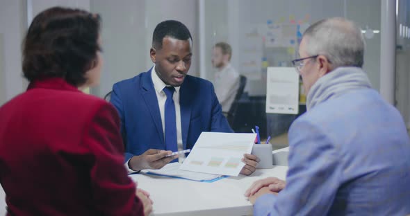 Afro American Male Bank Employee Telling Elderly Couple