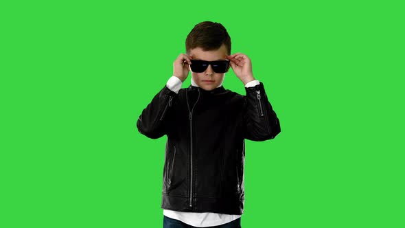 Young Boy in a Leather Jacket Putting on Black Glasses with Arms on His Hips on a Green Screen
