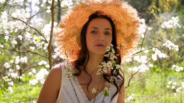 Brunette Woman with Long Hair in a Straw Hat Stands in the Apple Orchard