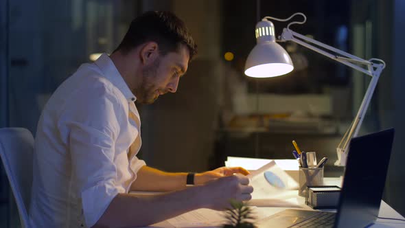 Businessman with Papers and Laptop at Night Office 4