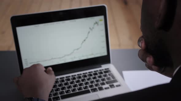 Young Businessman Analyzes the Financial Graph on a Laptop in the Office