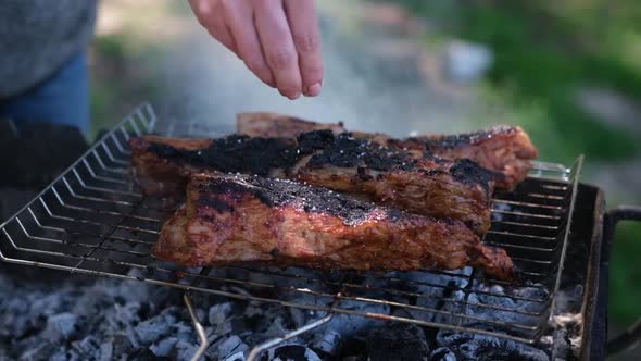 Salting Delicious Beef or Pork Ribs Frying on a Charcoal Grill