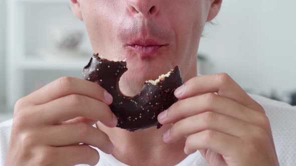 Man Eating Sweet Chocolate Donut Over White Interior Background