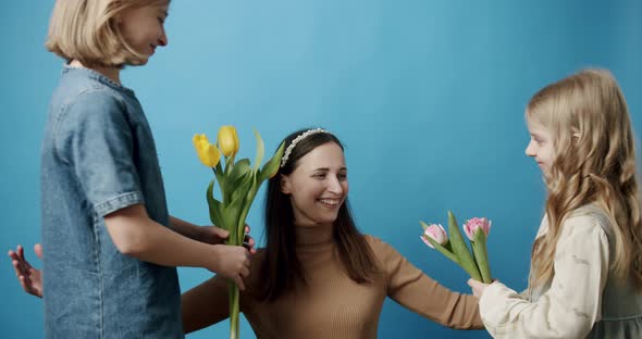 Sisters with Tulips Flowers Giving to Mom on a Blue Background Happy Mother