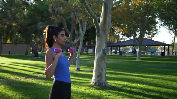 A beautiful and fit young hispanic woman in the park doing a dumbbell shoulder press workout exercis