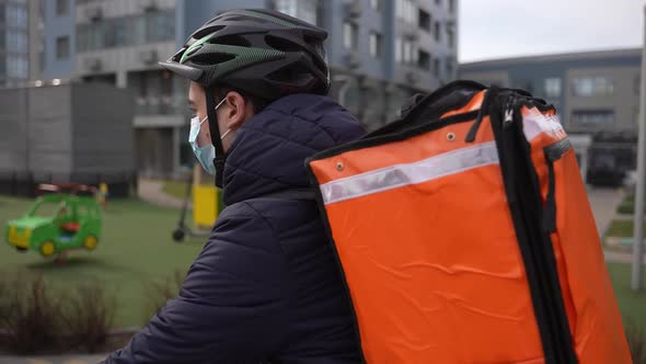 Food Courier in Face Mask Riding Bike Around City