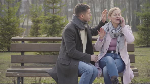 Adult Caucasian Blond Woman Talking on the Phone and Laughing As Younger Man Trying To Attract Her