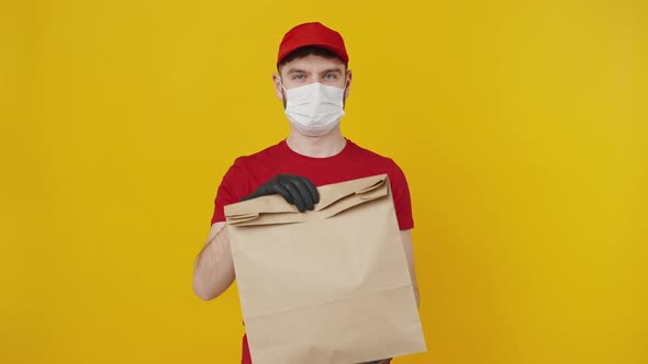 Young Delivery Man in Red Uniform Wearing Protective Medical Mask Offering Eco Paper Parcel to