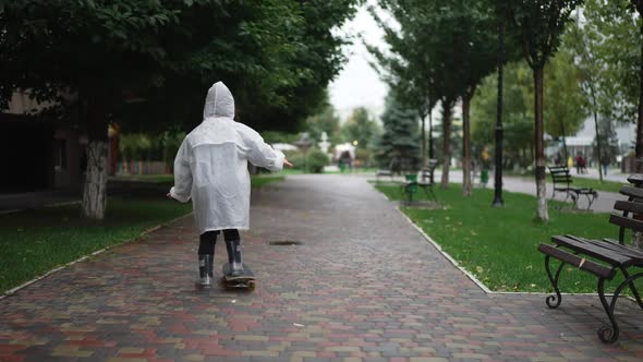 Live Camera Follows Joyful Little Person Riding Skateboard on Overcast Day on City Street