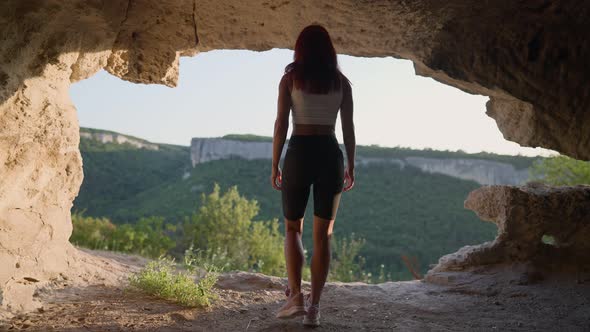 Slim Woman Traveler Dressed in Sportswear Walks Through Cave Moving Towards Exit