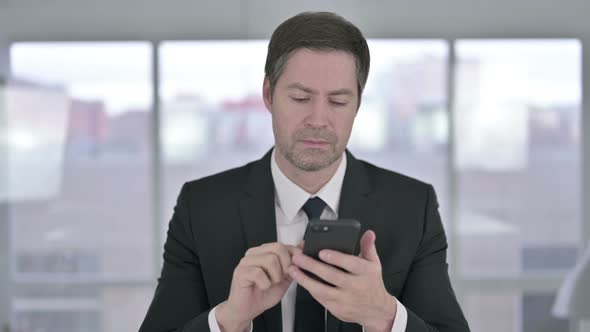 Cheerful Middle Aged Businessman Using Smartphone in Office