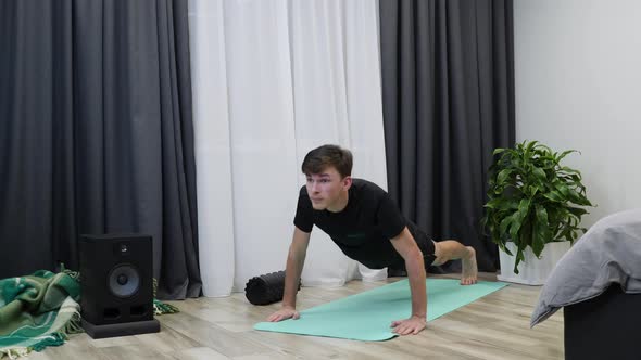 Young male athlete doing push-up exercises on yoga mat.