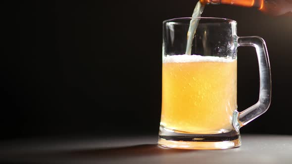 Refreshing Beer Pouring From Bottle Into Glass Mug Rotating Isolated at Black Background