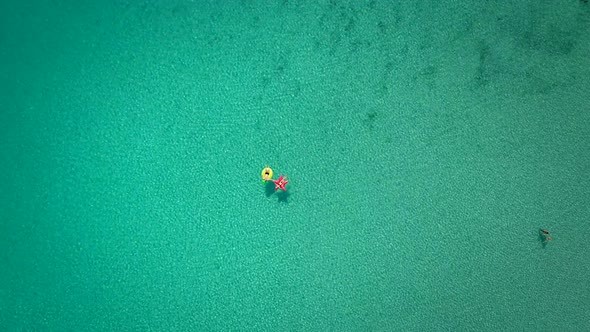 Aerial abstract view of two people floating in open sea on inflatables.