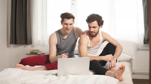 Cute Male Gay Couple Spend Time at Home. They Are Sitting Down on a Sofa and Use the Laptop.