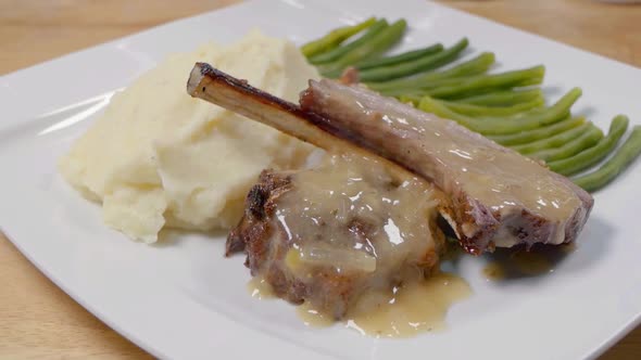 Slider Shot of Lamb Cutlets on a White Plate with Sauce, Mashed Potato and Green Beans