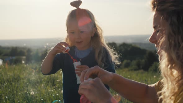 Little caucasian girl with mom playing with bubbles at the meadow. Shot with RED helium camera in 4K