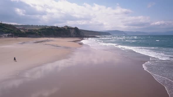 Smooth back direction drone view in Sopelana Beach. The wet sand reflects the clouds in the sky. In