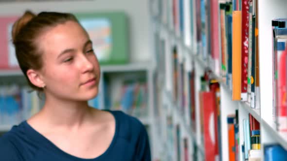 Schoolgirl selecting book from book shelf in library