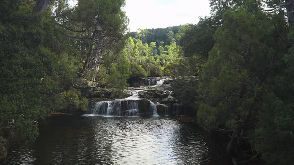 A long small rocky multi-level waterfall in a forest on a sunny day, wide shot