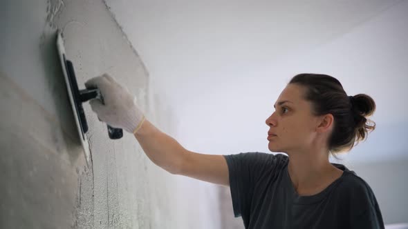 A Professional Repairwoman Puts a Plaster on the Wall with a Spatula