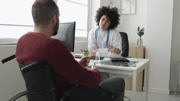 Doctor and Patient in Wheelchair Talking in a Medical Consultation in a Clinic