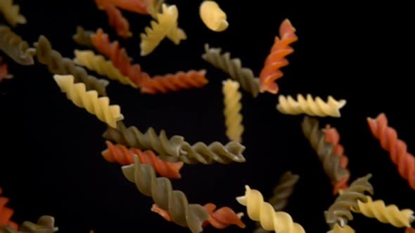 Dry Colored Pasta Fusili Flying Diagonally on a Black Background