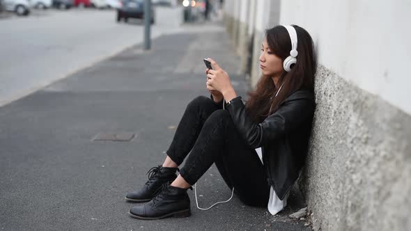 Young asiatic woman outdoor listening music using smartphone