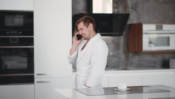 Portrait of Handsome Man in Bathrobe Talking on Cellphone at Kitchen in Morning