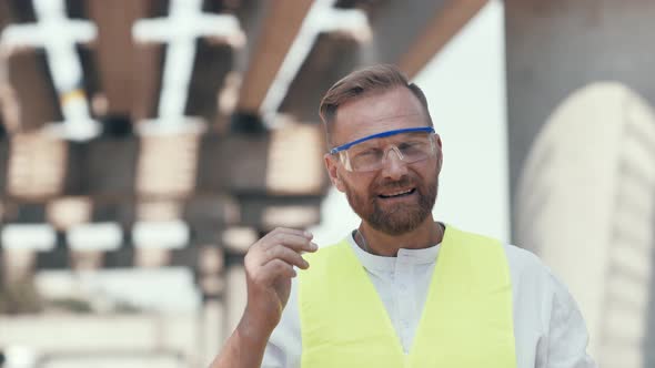 Close Up Portrait of Smiling Young Master Builder in Protective White Hard Hat Looking at Camera