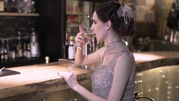 Closeup Portrait of a Young Attractive Woman in a 1920s Style Drink Wine or Champagne at the Bar