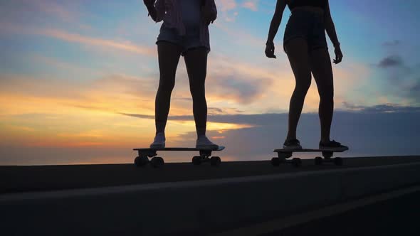 Close-up of the Legs of Two Girls Girlfriend in Shorts and Sneakers Ride Skateboards on the Slope