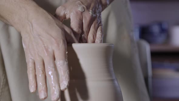 Male Hands of a Potter Form a Soft White Clay Pot Neck Turning It on a Potter's Wheel in a Creative